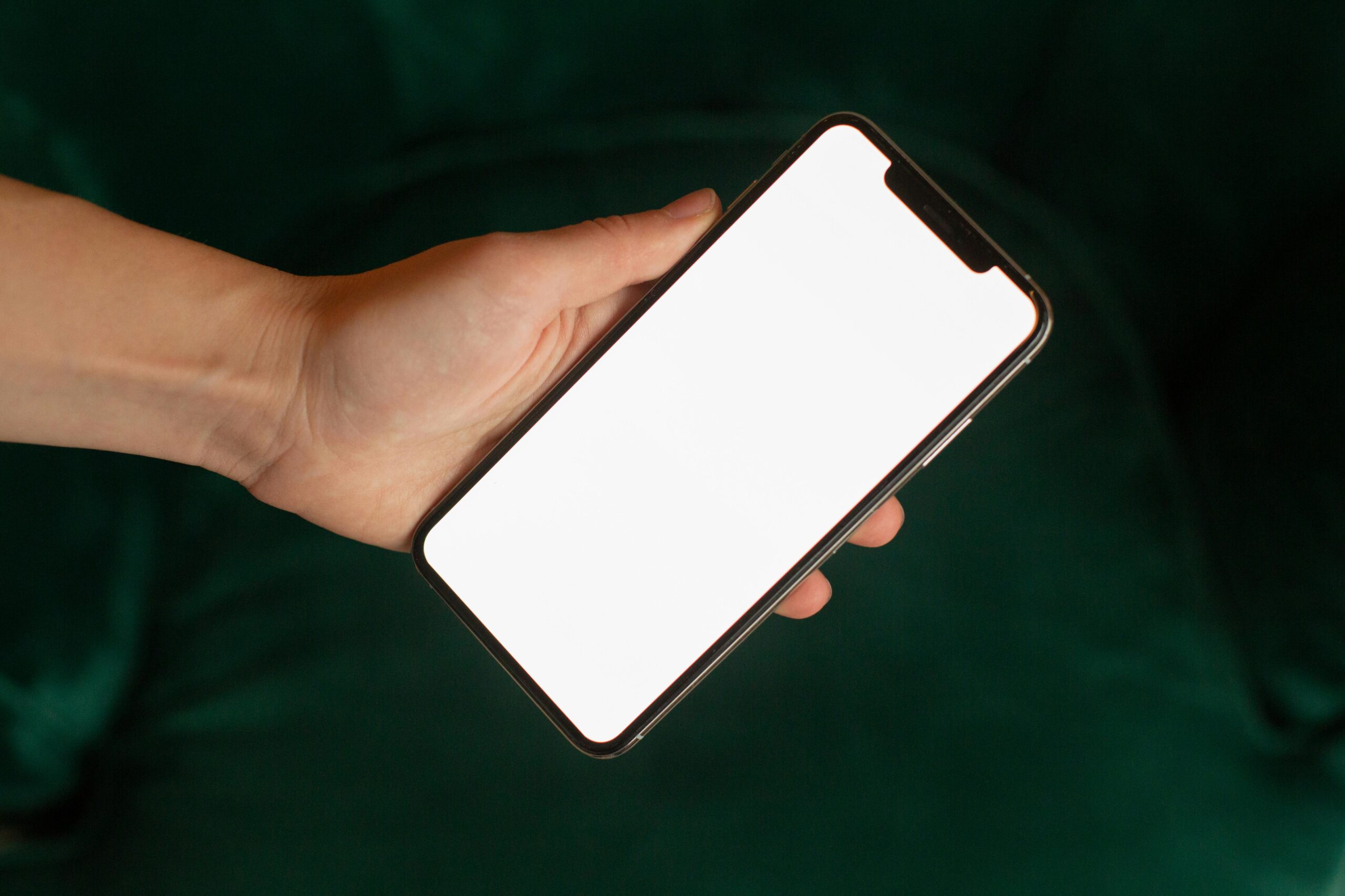 Hand holding a smartphone with a blank screen for mockup purposes.