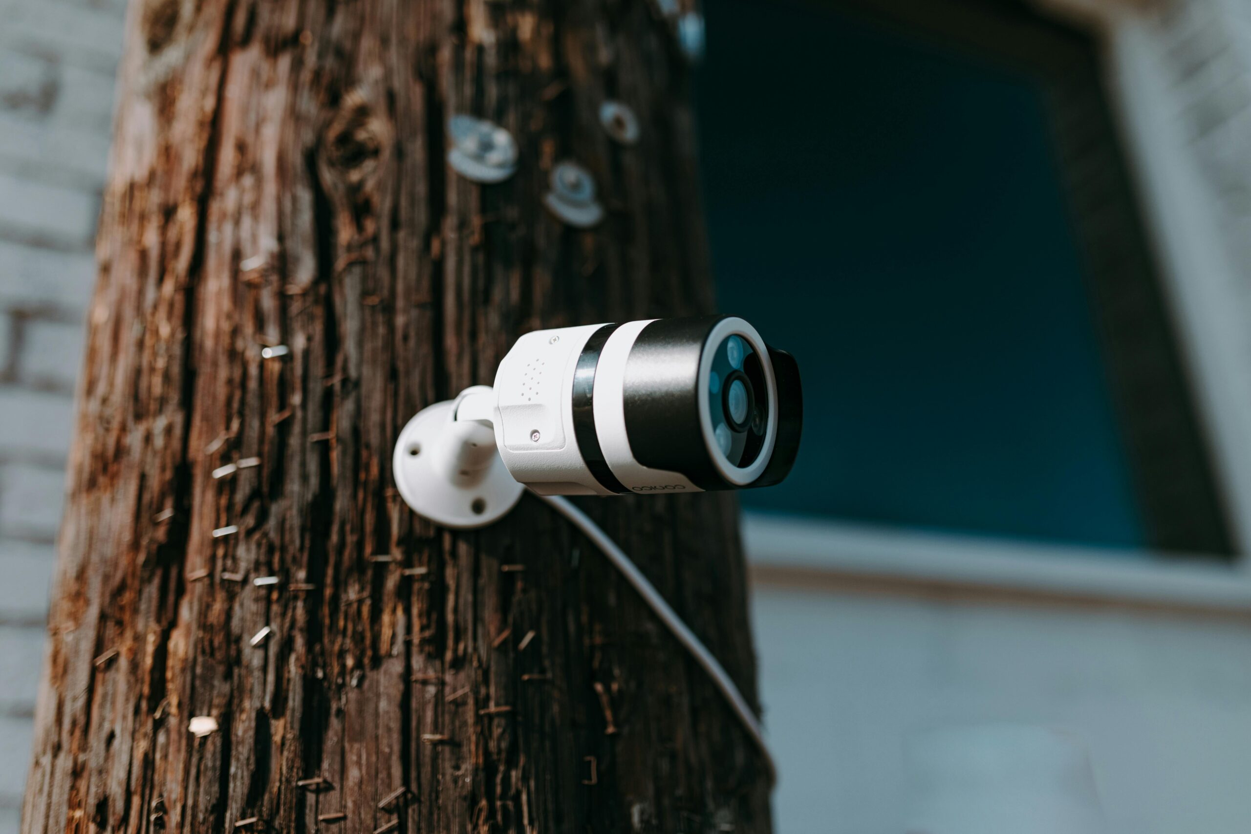 Close-up of a modern security camera mounted on a wooden post outdoors.