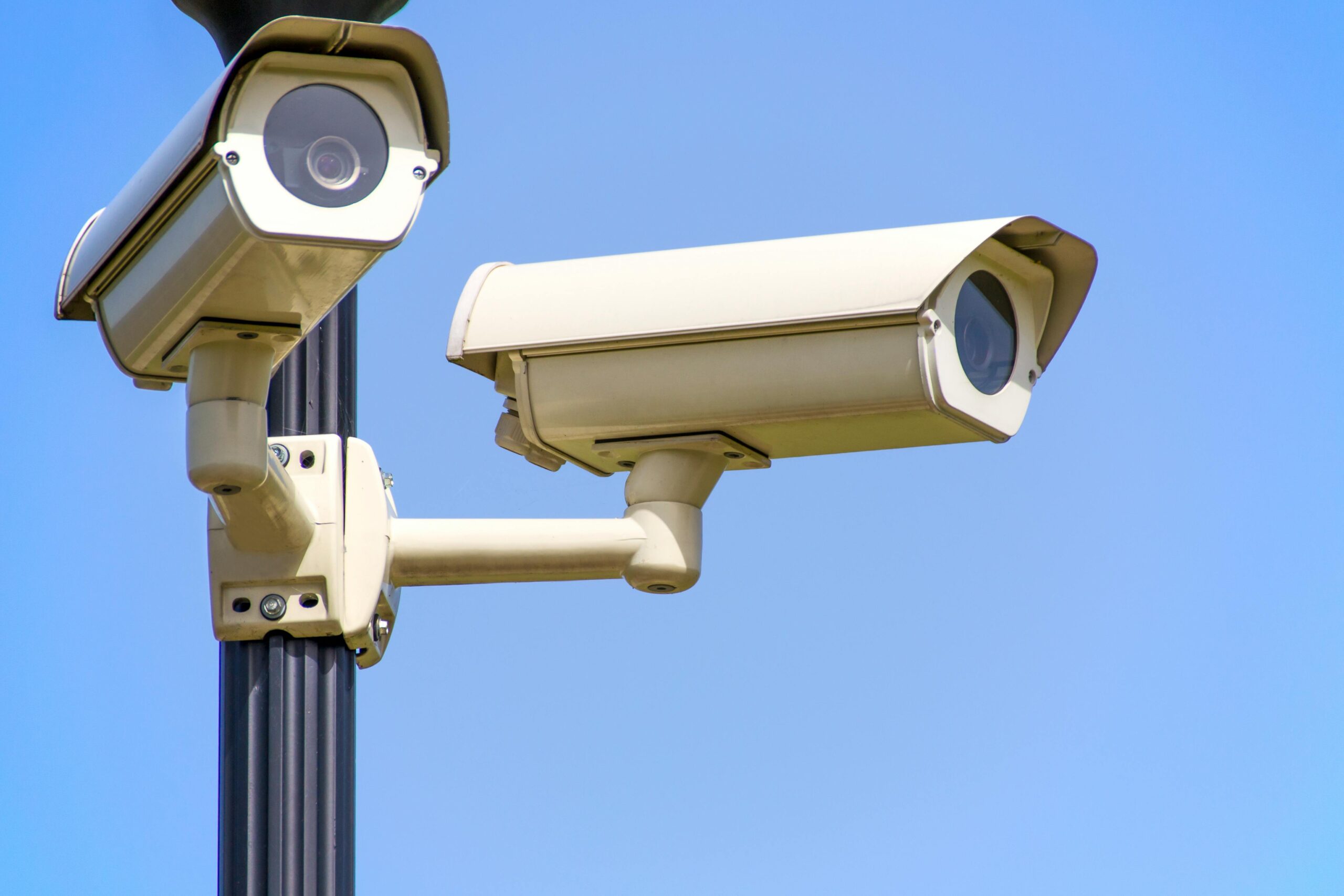 Outdoor security cameras mounted on a pole against a clear blue sky, ensuring vigilant surveillance.